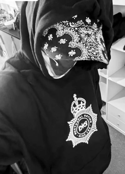 Person wearing a black hoodie with a Nocturnal Notice logo and bandana, indoors.
