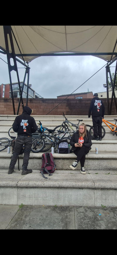 People sitting on steps with bicycles in the background wearing nocturnal notion hoodies on a cloudy day.